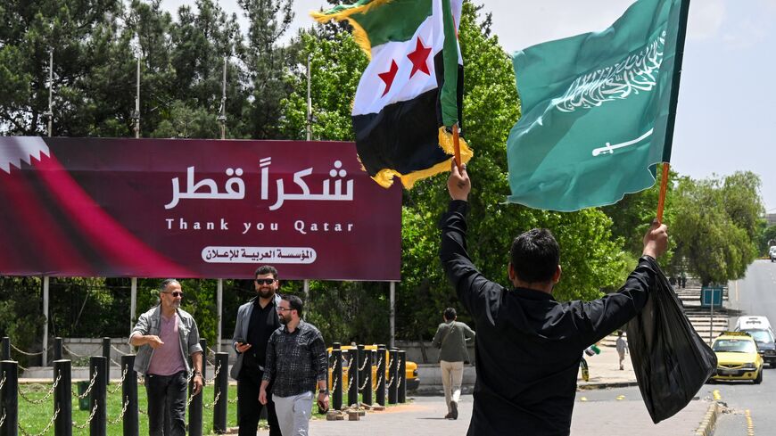 A man carries the Syrian and the Saudi flags past a billboard thanking Qatar, in Damascus, on May 14, 2025.