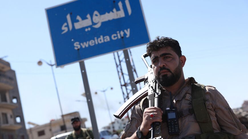 A member of Syria's security forces stands under a sign in the predominantly Druze city of Sweida (Suwayda), on July 15, 2025, following clashes between Bedouin tribes and Druze fighters. 