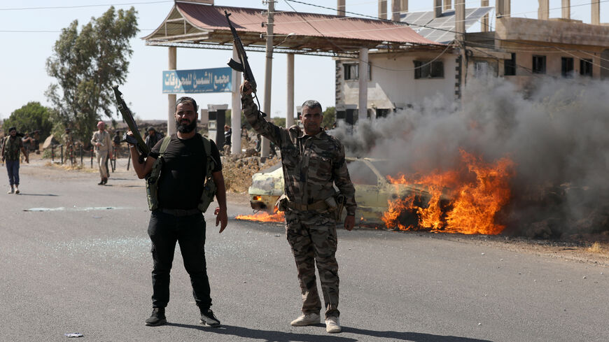 Two armed men gesture as a car burns near the site of clashes between Druze and Bedouin factions on July 14, 2025 in Suwayda, Syria.