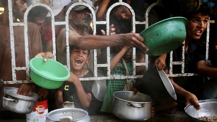 Palestinians shove to receive a hot meal at a charity kitchen in the Mawasi area of Khan Yunis in the southern Gaza Strip on July 22, 2025.