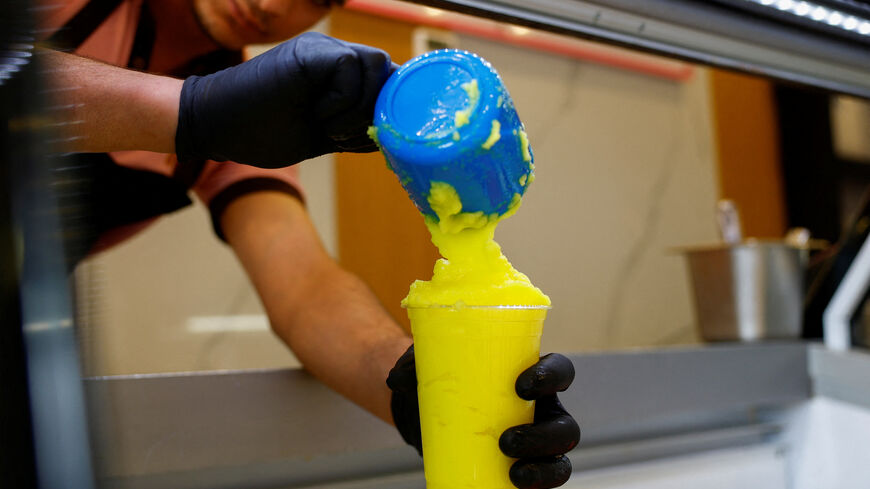 A worker fills a cup of "Barrad", a traditional Palestinian slushy drink with citrus flavours, at a newly opened branch of an ice cream shop that was partially destroyed in Gaza during the ongoing conflict between Israel and Hamas, in Ajman, United Arab Emirates, August 19, 2025. REUTERS/Raghed Wake