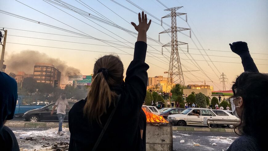 Iranian women without wearing hijab shout slogans while gathering around a burning dumpster during a protest near Punak square, on Oct. 1, 2022