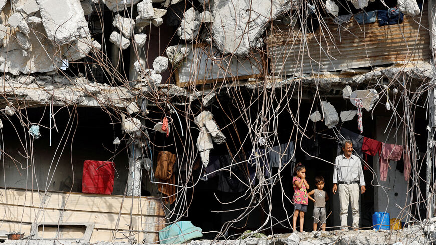 A Palestinian man and children stand at a heavily damaged building surrounded by rebar and rubble, amid a ceasefire between Israel and Hamas, in Gaza City, November 2, 2025. REUTERS/Mahmoud Issa