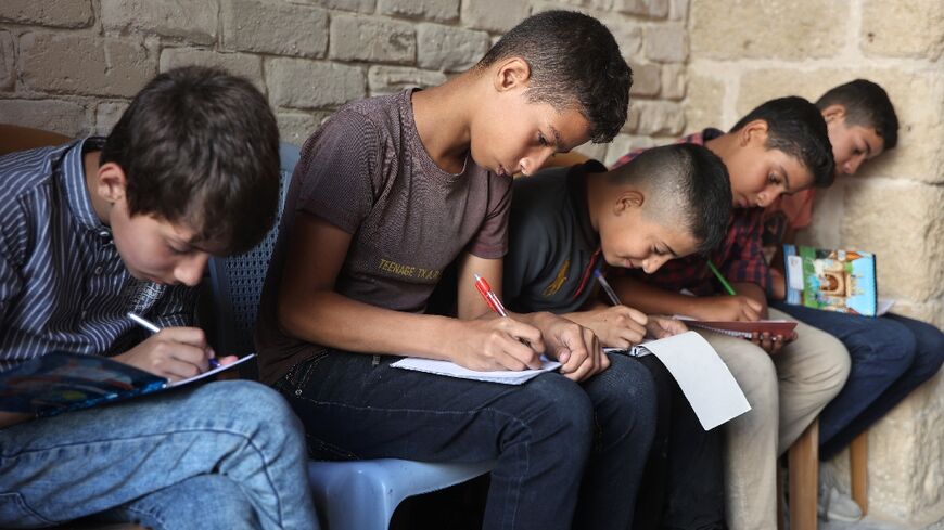 Palestinian children take notes as they attend a class in the historic Al-Kamaliya al-Othmanya school in Gaza City's Old Town, as part of a volunteer initiative organised by displaced teachers, in Gaza City