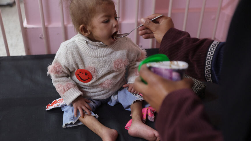 Arjwan Al-Dahini, a Palestinian child, who doctors say suffers from severe acute malnutrition, sits on a hospital bed while being fed by her mother, at Nasser Hospital in Khan Younis, southern Gaza Strip, December 16, 2025. REUTERS/Ramadan Abed