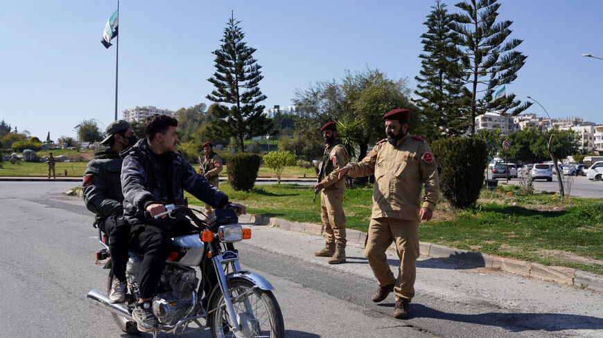 FILE PHOTO: A member of Syrian security forces speaks with men on a motorbike in Latakia, Syria, March 11, 2025. REUTERS/Karam al-Masri/File Photo