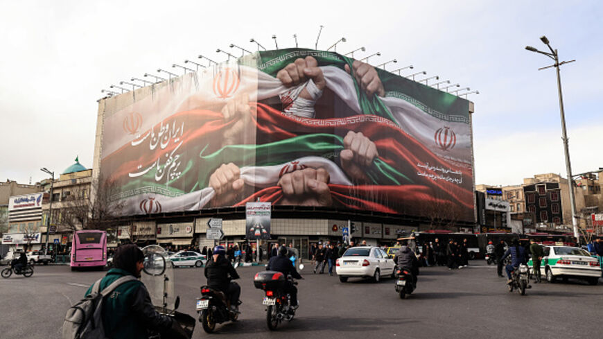 Vehicles pass by a large patriotic banner depicting the Iranian flag on Enghelab Square in Tehran on January 14, 2026. (ATTA KENARE / AFP via Getty Images