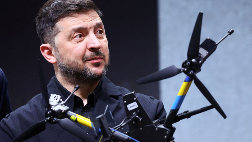 Ukrainian President Volodymyr Zelenskiy reacts as he is pictured behind a drone during his visit to a facility of German drone maker Quantum Systems, on the sidelines of the annual Munich Security Conference (MSC), near Munich, Germany, February 13, 2026. REUTERS/Thilo Schmuelgen