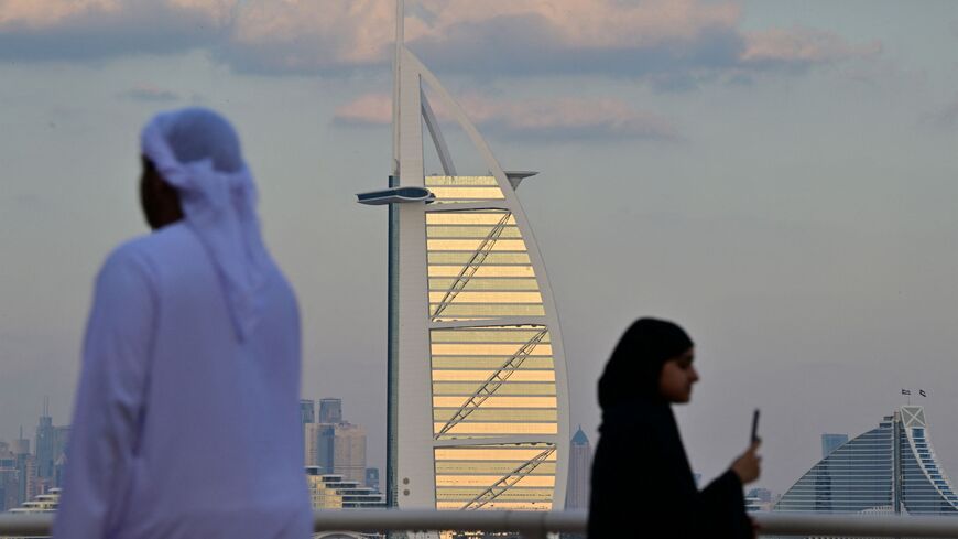 A man and woman walk along a promenade overlooking the Burj al-Arab and Dubai skyline on January 4, 2025. (Photo by Giuseppe CACACE / AFP) (Photo by GIUSEPPE CACACE/AFP via Getty Images)