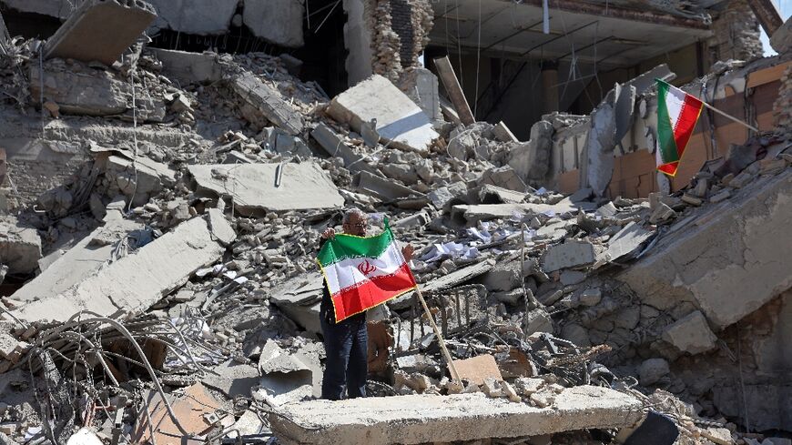 A man holds an Iranian flag amid the debris of a destroyed building following airstrikes in central Tehran on March 4, 2026