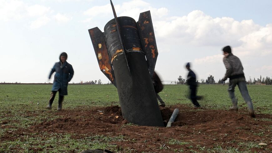 Children play around an unexploded missile that landed in an open field on the outskirts of Qamishli, eastern Syria