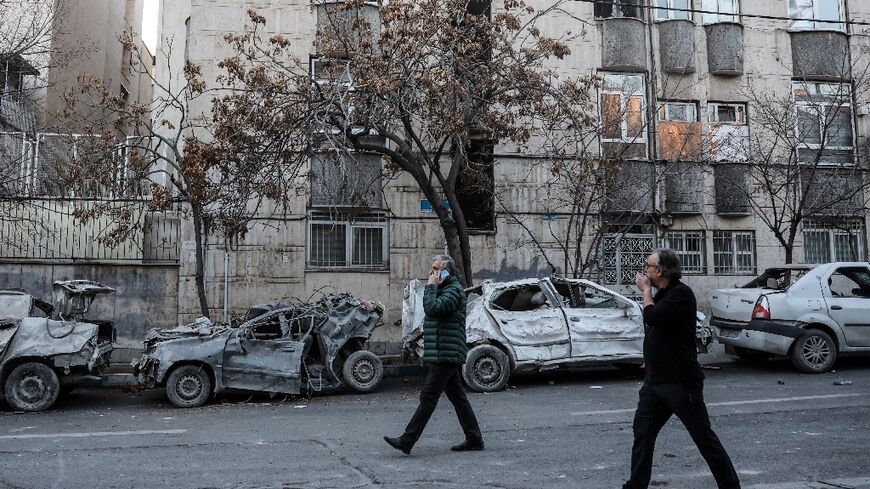 A man on a phone walks past the wreckage of cars beside damaged residential buildings near Niloufar square in Tehran 