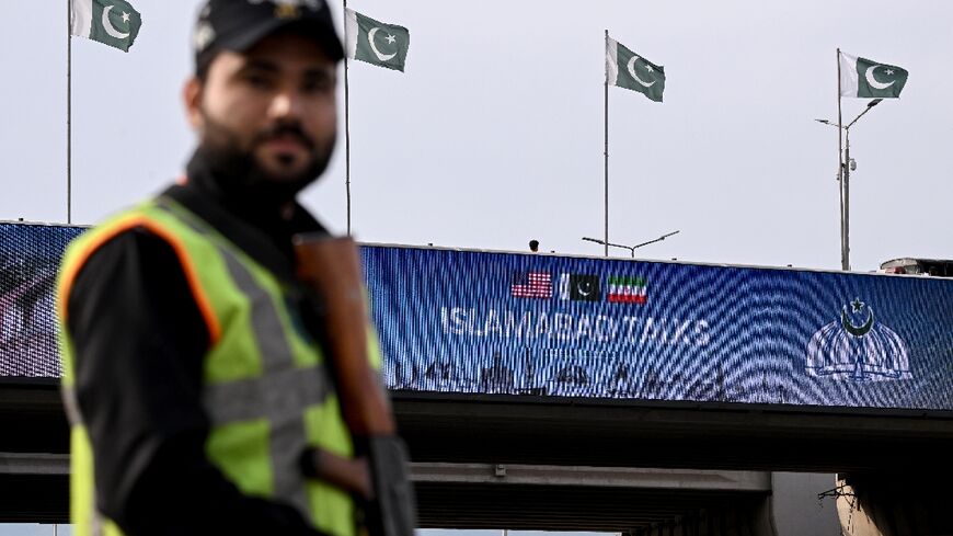 A policeman stands guard in front of a digital screen displaying news of US–Iran peace talks along a road in Pakistan's capital Islamabad