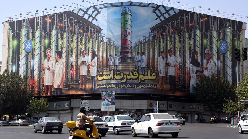 Iranians drive next to a billboard displaying pictures of nuclear scientists, centrifuges and a sentence reading in Farsi "Science is the power," at Enqelab Square in Tehran, on Aug. 29, 2025. 