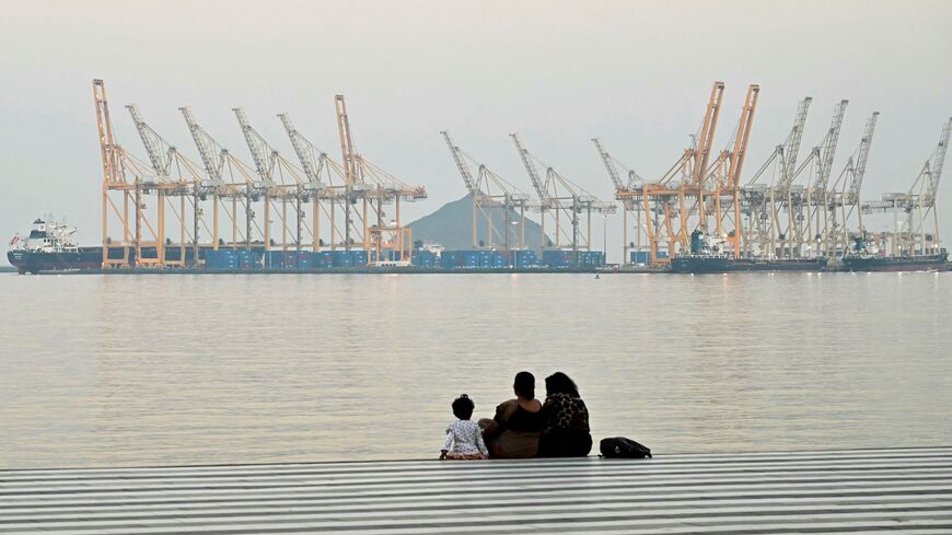 A family sits against the backdrop of a dockyard in Khor Fakkan in the Gulf emirate of Sharjah, off the coast of the Gulf of Oman, on Feb. 25, 2026. 