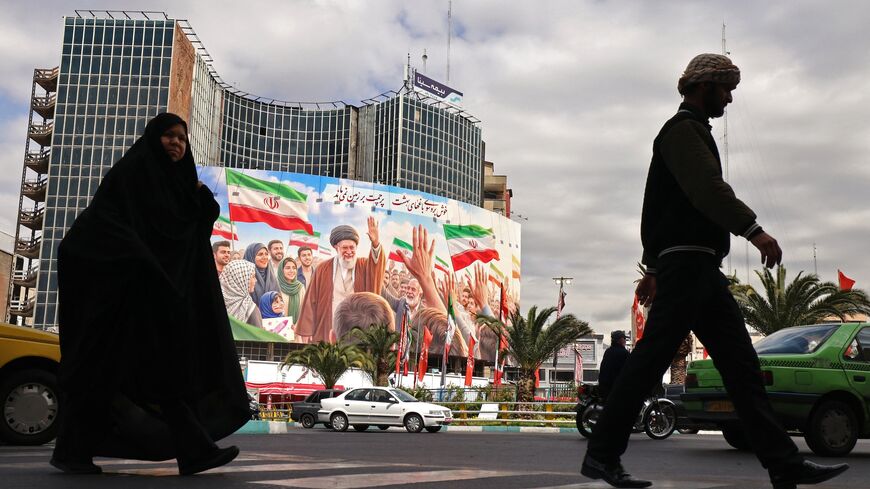 Commuters make their way past a giant billboard of slain Iranian supreme leader Ayatollah Ali Khamenei at Valiasr Square in Tehran on April 19, 2026. 