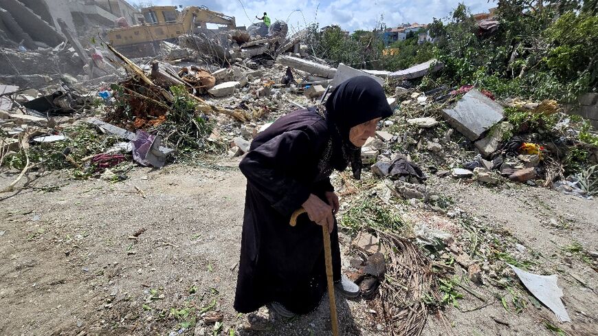 A woman walks past Lebanese rescuers searching through the rubble in the southern village of Deir Qanun al-Nahr, a day after an Israeli strike
