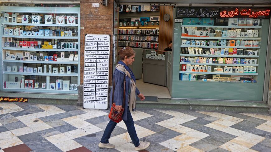 An Iranian woman walks past a mobile phone shop at the Valiasr Square in Tehran on April 19, 2026. 