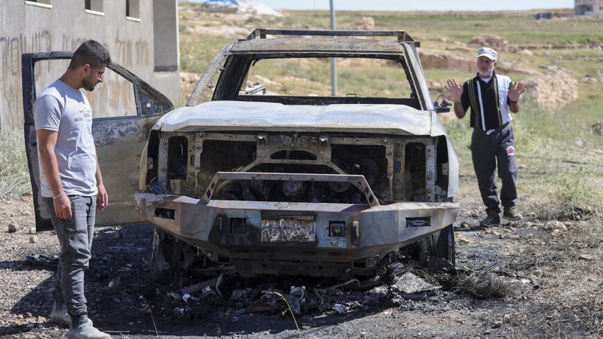 Two men stand next to the burned remains of a Palestinian vehicle in the Wadi al-Rakhim area of Susya village in Masafer Yatta, south of Hebron in the Israeli-occupied West Bank, on May 1, 2026. 