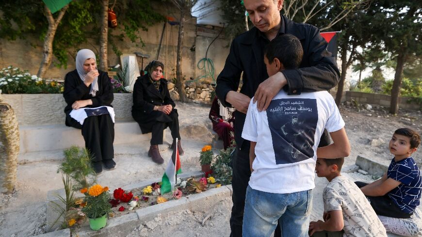 Sameh Shtayyeh, father of 15-year-old Youssef who was killed by Israeli soldiers, hugs another son as they visit Youssef's grave in the village of Till, west of Nablus, in the West Bank