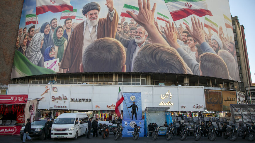A police officer stands holding a flag in Valiasr Square beneath a mural of the late Ayatollah Ali Khamenei on April 23, 2026 in Tehran, Iran. 