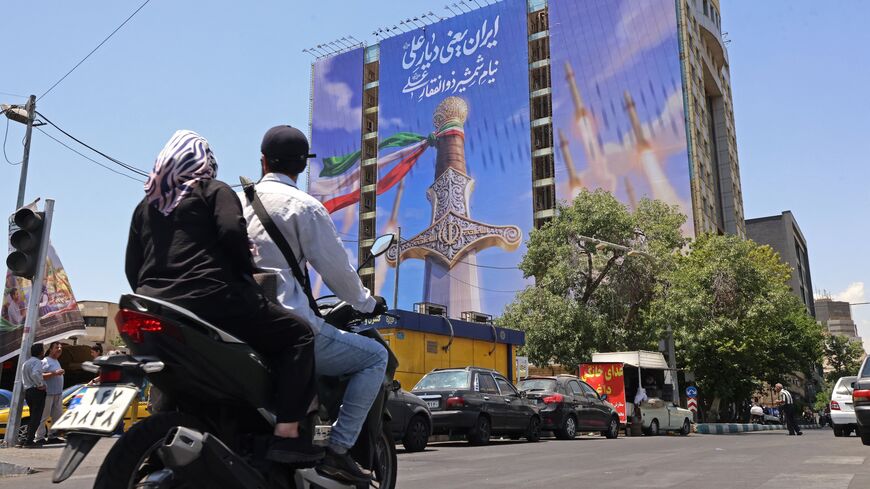 Motorists ride past a giant banner depicting Iranian missiles and a sword belonging to Imam Ali, the first Imam of the Shiites, at the Vanak Square in Tehran on June 10, 2026. 