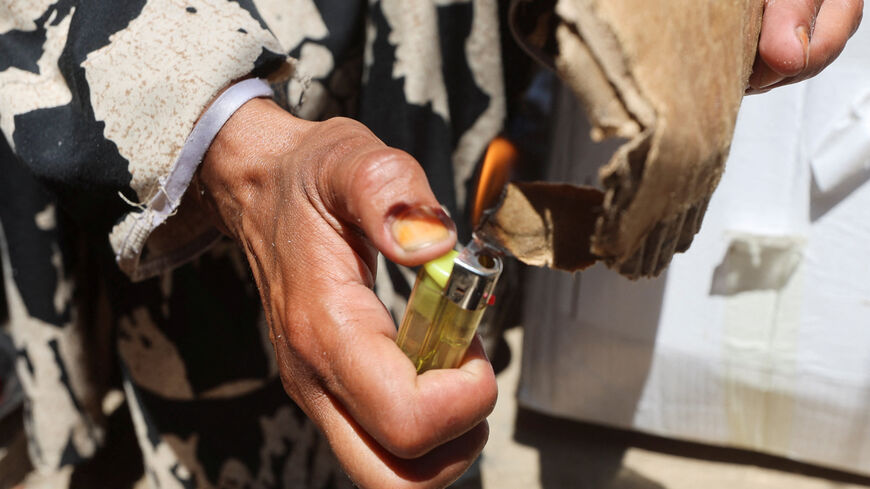 Displaced Palestinian woman Nisreen Abu Saada uses a lighter to ignite cardboard to start a fire outside her tent, amid shortages of lighters and cooking gas, in Khan Younis, in the southern Gaza Strip, July 21, 2026. REUTERS/Ramadan Abed