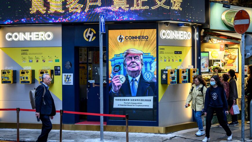 People walk past a cryptocurrency exchange office with a screen featuring US President Donald Trump holding cryptocurrency coins in Hong Kong on March 12, 2025.