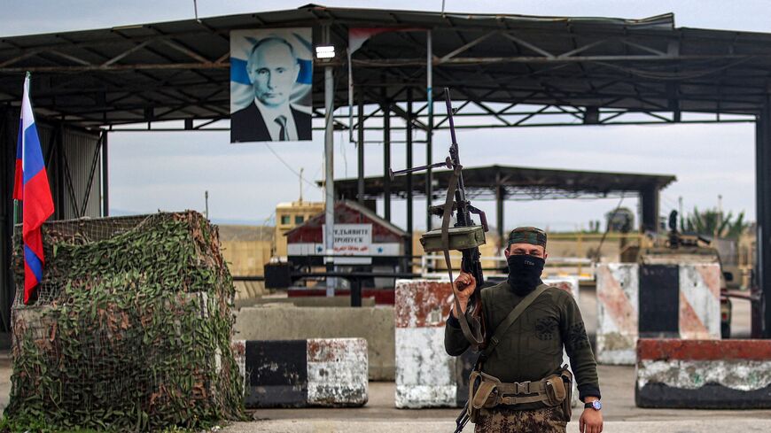 A Syrian rebel fighter looks on as he stands at an inspection checkpoint for incoming vehicles before a Russian flag and Russian soldiers behind manning the entrance of the Russian-leased Syrian military base of Hmeimim in Latakia province in western Syria on Dec. 29, 2024. 