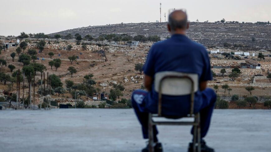 A Palestinian man sits on the rooftop of his house as he looks at a newly established Israeli settler outpost in Burqah in the Israeli-occupied West Bank