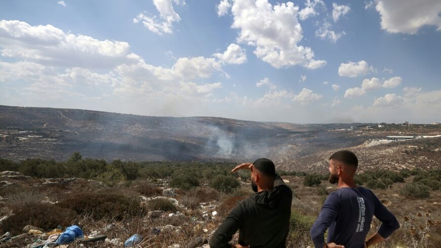 Palestinians stand on a hilltop looking down at the smoke from fires after Israeli soldiers fired tear gas at the olive harvest near the village of Asira al-Qibliya on October 3, 2026