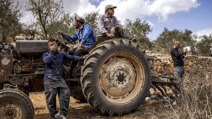 Palestinian men sitting in and by a tractor look on after another man was injured by gunfire whilst being chased away by Israeli forces, in Aqraba in the Israeli-occupied West Bank on Oct. 6, 2026.