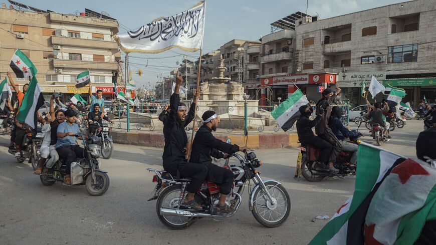 Demonstrators ride through a street while waving Syrian flags