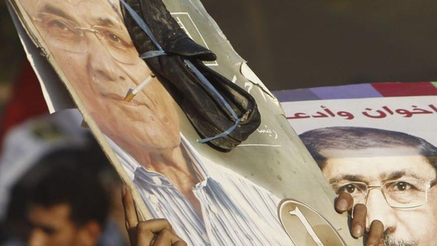 Supporters of Muslim Brotherhood's president-elect Mohamed Morsy holds up a poster of Morsy next to a defaced poster of candidate Ahmed Shafik at Tahrir Square in Cairo June 24, 2012. Morsy pledged on Sunday to be a president for all Egyptians in a televised address after the Islamist was declared the winner of last weekend's election - an event he called a "historic moment". REUTERS/Amr Abdallah Dalsh  (EGYPT - Tags: POLITICS ELECTIONS)
