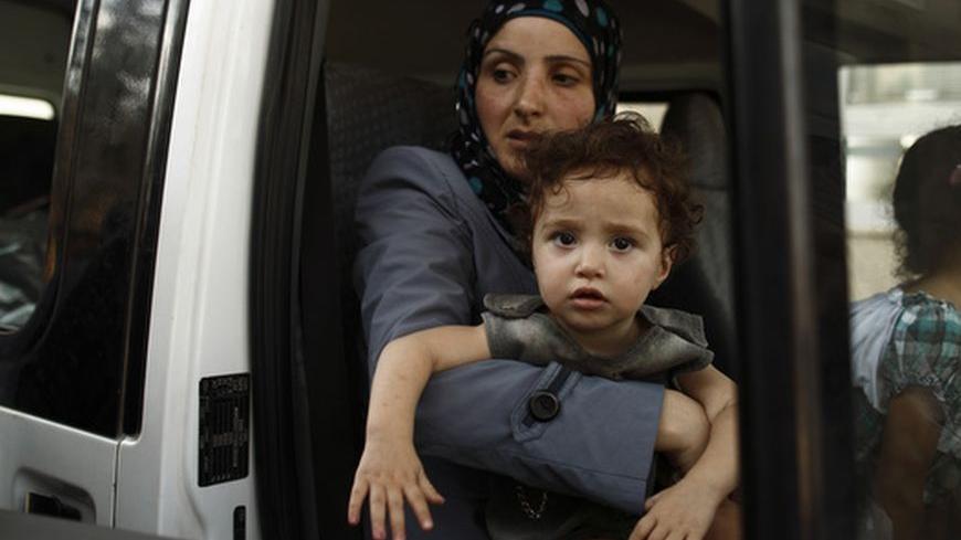 A Syrian woman carries her daughter as their family are about to cross back into Syria at the Turkish Cilvegozu border, opposite the Syrian commercial crossing point Bab al-Hawa, in Reyhanli, Hatay province, July 25, 2012. The Syrian family of five travelling back to Syria said they prefer risking death in their home country rather than stay in Turkey. Turkey has closed its border gates with Syria to commercial traffic due to worsening security conditions but will keep them open for refugees fleeing the Syr