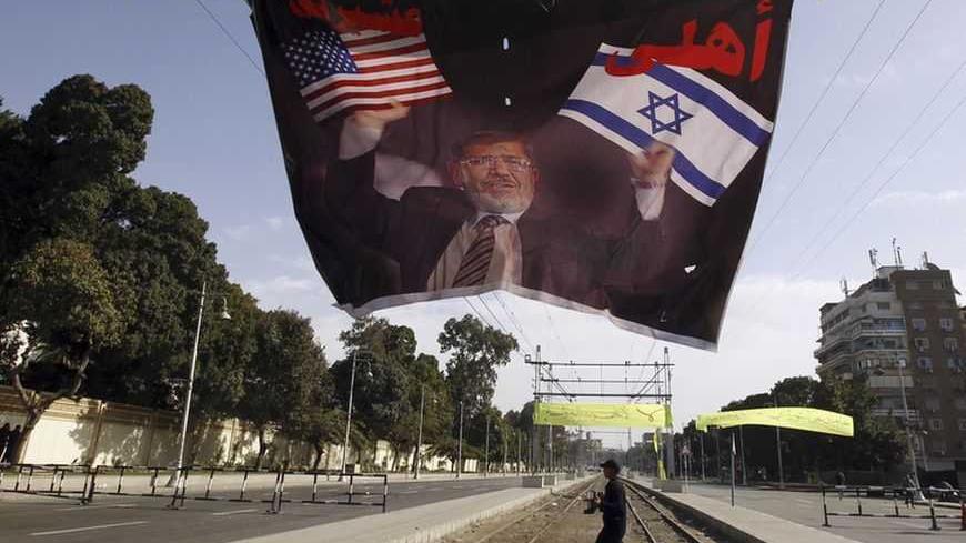 A riot police officer walks under a banner depicting Egyptian President Mohamed Mursi holding the Israeli and American flags in each hand, reading: 'My family (Israel) and my clan (U.S.)' at the presidential palace in Cairo January 25, 2013. Hundreds of youths fought Egyptian police in Cairo on Friday on the second anniversary of the revolt that toppled Hosni Mubarak and brought the election of an Islamist president who protesters accuse of riding roughshod over the new democracy. Opponents of Mursi and his