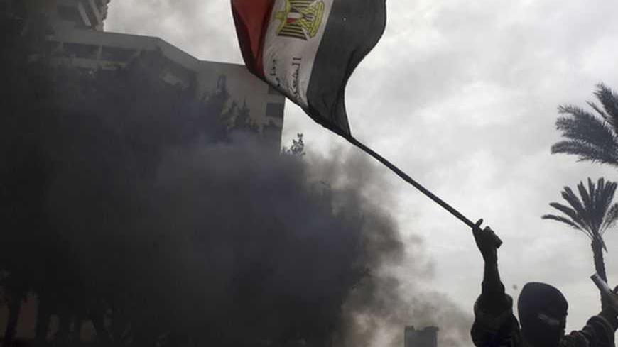 A protester opposing Egyptian President Mohamed Mursi gestures with a national flag at riot police during clashes along Qasr Al Nil bridge leading to Tahrir Square in Cairo January 28, 2013. A man was shot dead on Monday in a fifth day of violence in Egypt that has killed 50 people and prompted the Islamist president to declare a state of emergency in an attempt to end a wave of unrest sweeping the Arab world's biggest nation. REUTERS/Amr Abdallah Dalsh (EGYPT - Tags: POLITICS CIVIL UNREST TPX IMAGES OF THE