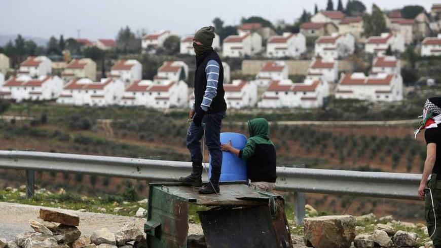 The Jewish settlement of Halamish is seen in the background as a stone-throwing Palestinian protester stands on a garbage bin during clashes with Israeli security officers at a weekly protest against the settlements, in the West Bank village of Nabi Saleh, near Ramallah February 1, 2013. U.N. human rights investigators called on Israel on Thursday to halt settlement expansion and withdraw all half a million Jewish settlers from the occupied West Bank, saying that its practices could be subject to prosecutio