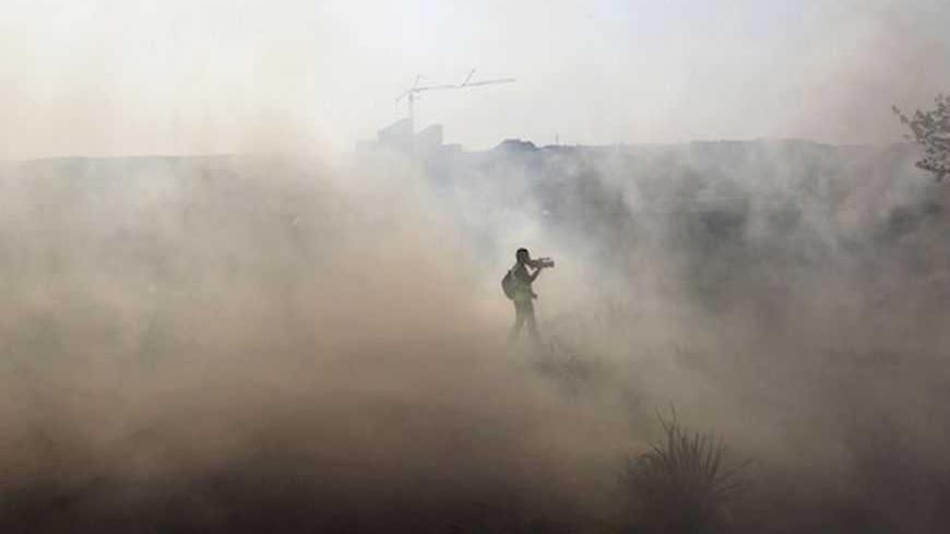 A journalist walks through tear gas fired by Israeli security officers (unseen) during clashes with stone-throwing Palestinians following a rally marking the 48th anniversary of the founding of the Fatah movement, in the West Bank village of Bilin near Ramallah January 4, 2013. REUTERS/Ammar Awad (WEST BANK - Tags: POLITICS CIVIL UNREST) - RTR3C3NU
