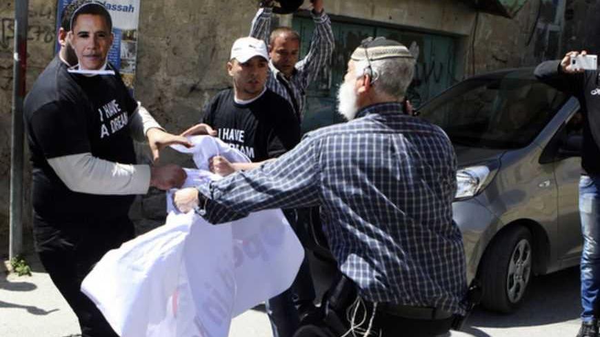 An Israeli settler (front) and Palestinians demonstrators, one wearing a mask depicting U.S. President Barack Obama, scuffle during a protest against the continued closure by the Israeli army of Shuhada street to Palestinians in the West Bank city of Hebron March 20, 2013. Obama arrived in Israel on Wednesday without any new peace initiative to offer disillusioned Palestinians and facing deep Israeli doubts over his pledge to prevent a nuclear-armed Iran. REUTERS/ Mussa Qawasma (WEST BANK - Tags: POLITICS C