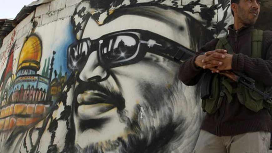 A gunman stands near a picture of late Palestinian leader Yasser Arafat at Ain al-Hilweh Palestinian refugee camp near the port city of Sidon in south Lebanon March 12, 2013. Ten people were wounded and one killed during clashes between the Fatah movement and radical Islamists that started on Monday.  REUTERS/Ali Hashisho (LEBANON - Tags: POLITICS CIVIL UNREST) - RTR3EW3X