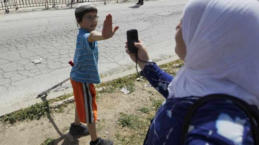 A Jewish boy lifts his hand to prevent a Palestinian from taking his picture near a police barrier cordoning off a building the day after Israeli police evicted Jewish settlers who occupied it in the West Bank city of Hebron April 5, 2012. Israeli police evicted Jewish settlers on Wednesday from the building they said they had bought from a Palestinian in the heart of Hebron, a frequent flashpoint in the Israeli-Palestinian conflict. REUTERS/Ammar Awad (WEST BANK - Tags: POLITICS MILITARY CIVIL UNREST) - RT