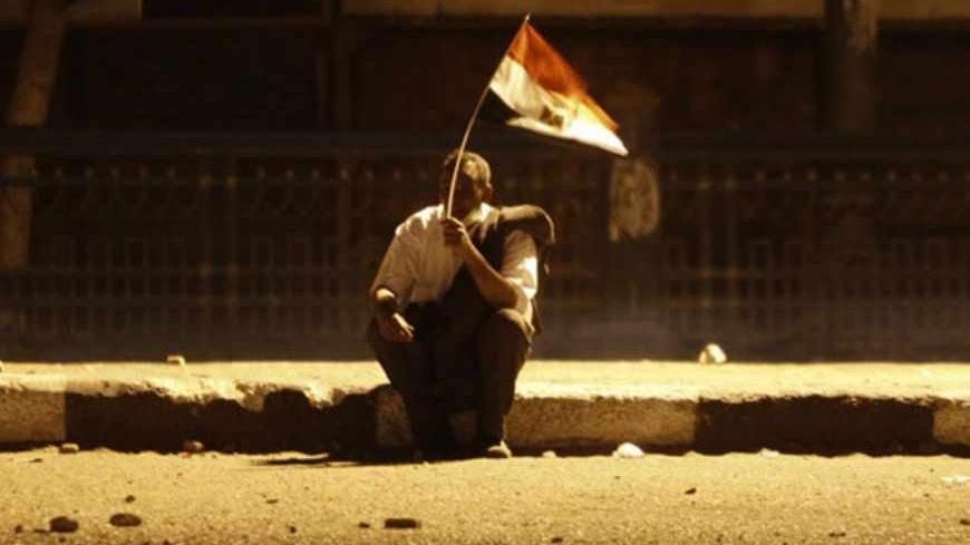 A protester opposing Egyptian President Mohamed Mursi gestures at the riot police while holding a national flag during clashes with Islamist protesters in front of The 6th October Bridge near Tahrir Square in Cairo, April 19, 2013. Thousands of Islamist protesters clashed with opponents as they rallied on Friday to demand a purge of Egypt's judiciary, a sign of rising tension between the Islamist government and legal organs seen as a redoubt of old regime influence. REUTERS/Amr Abdallah Dalsh (EGYPT - Tags: