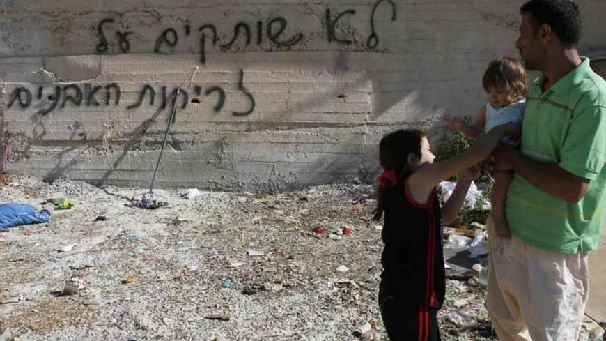 Palestinians stand next to graffiti sprayed on a wall near their house in the Arab neighborhood of Beit Hanina in East Jerusalem June 24, 2013. Graffiti was sprayed and tires were slashed on 21 cars overnight in Beit Hanina in what appeared to be another in a series of "Price Tag" attacks by suspected Jewish militants. Police opened an investigation. The graffiti reads: We will not remain silent in the face of the stone-throwing". REUTERS/Ammar Awad (JERUSALEM - Tags: POLITICS CIVIL UNREST) - RTX10YSG