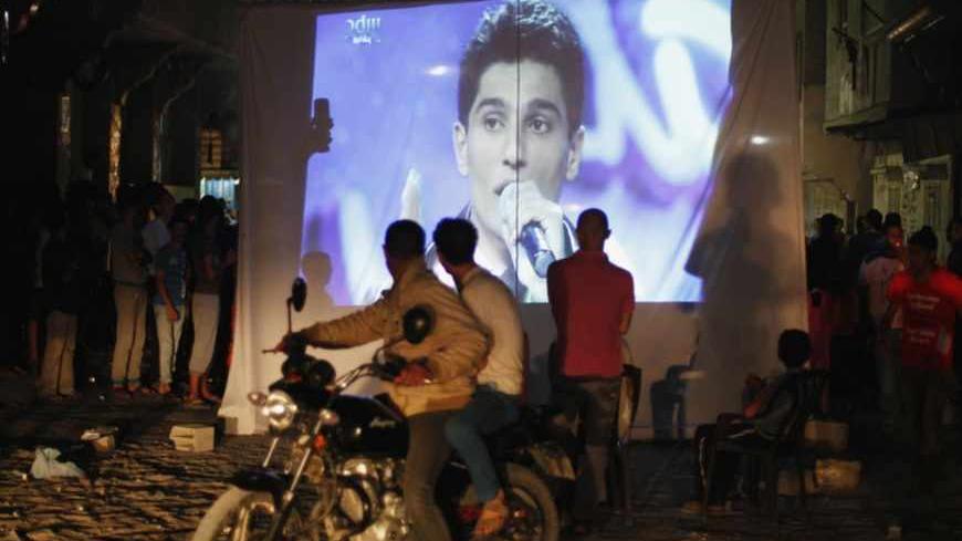 People watch Palestinian singer Mohammed Assaf as he sings in Beirut during the "Arab Idol" program, in Khan Younis in the southern Gaza Strip June 22, 2013. The 22-year-old singer Mohammed Assaf, from the Gaza Strip, was named the winner of "Arab Idol" in a TV talent contest in Beirut. REUTERS/Ibraheem Abu Mustafa (GAZA - Tags: SOCIETY ENTERTAINMENT) - RTX10XJ1