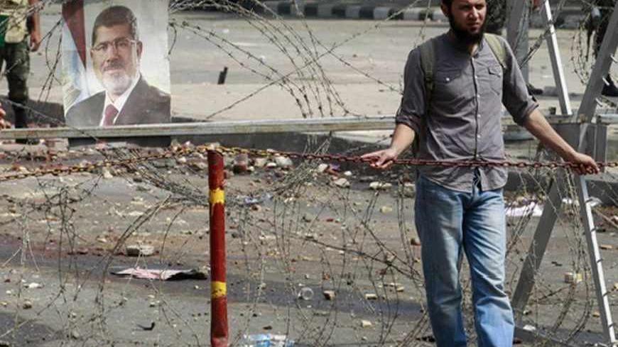 A supporter of deposed Egyptian President Mohamed Mursi stands behind concertina wire outside the Republican Guard headquarters in Cairo July 9, 2013. Egypt's interim President Adli Mansour on Tuesday named liberal economist and former finance minister Hazem el-Beblawi as prime minister in a transitional government, as the authorities sought to steer the country to new parliamentary and presidential elections. REUTERS/Louafi Larbi (EGYPT - Tags: POLITICS CIVIL UNREST) - RTX11I1R