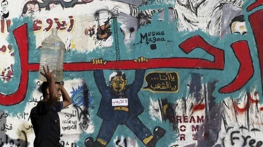 A man carrying a water container on his head walks in front of a wall filled with graffiti depicting deposed Egyptian President Mohamed Mursi with a message reading "Leave", at Tahrir Square in Cairo July 14, 2013. Egypt's interim prime minister filled senior posts on Sunday in a cabinet that will lead the country under an army-backed "road map" to restore civilian rule following overthrow of Mursi.   REUTERS/Amr Abdallah Dalsh  (EGYPT - Tags: POLITICS CIVIL UNREST) - RTX11MQ5