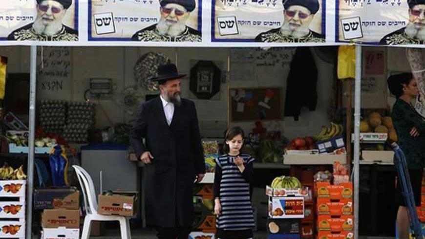 An ultra-Orthodox Jewish man stands beneath campaign posters depicting Rabbi Ovadia Yosef, the spiritual leader of the ultra-Orthodox Shas party, in the southern city of Ashdod January 17, 2013. A fixture in successive governments, Shas, the ultra-Orthodox party draws its support from the fast-growing community of religious Jews of Middle Eastern origin whose spiritual leader is the 92-year-old, Iraqi-born rabbi Ovadia Yosef. According to opinion polls, it will maintain its 11 seats in parliament. REUTERS/A