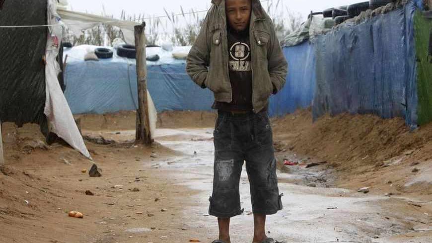 A Syrian refugee boy shields himself from the rain with his jacket at a refugee camp in the city of Tyre in southern Lebanon January 31, 2013. Donor countries have pledged more than $1.5 billion to aid Syrians stricken by civil war, U.N. Secretary-General Ban Ki-moon said on Wednesday after warning that the conflict had wrought a catastrophic humanitarian crisis. REUTERS/Ali Hashisho (LEBANON - Tags: POLITICS CIVIL UNREST TPX IMAGES OF THE DAY) - RTR3D6R0