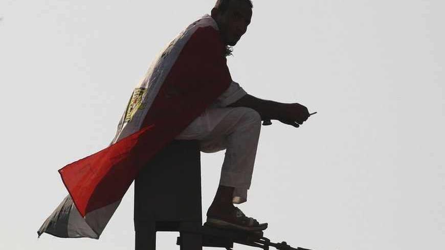 A supporter of Muslim Brotherhood and ousted Egyptian President Mohamed Mursi wrapped in an Egyptian flag sits on top of power pole during a protest in Cairo August 23, 2013. Mass protests called by Egypt's Muslim Brotherhood mostly failed to materialise on Friday as the movement reeled from a bloody army crackdown on followers of Mursi. REUTERS/Muhammad Hamed (EGYPT - Tags: POLITICS CIVIL UNREST) - RTX12UJ2